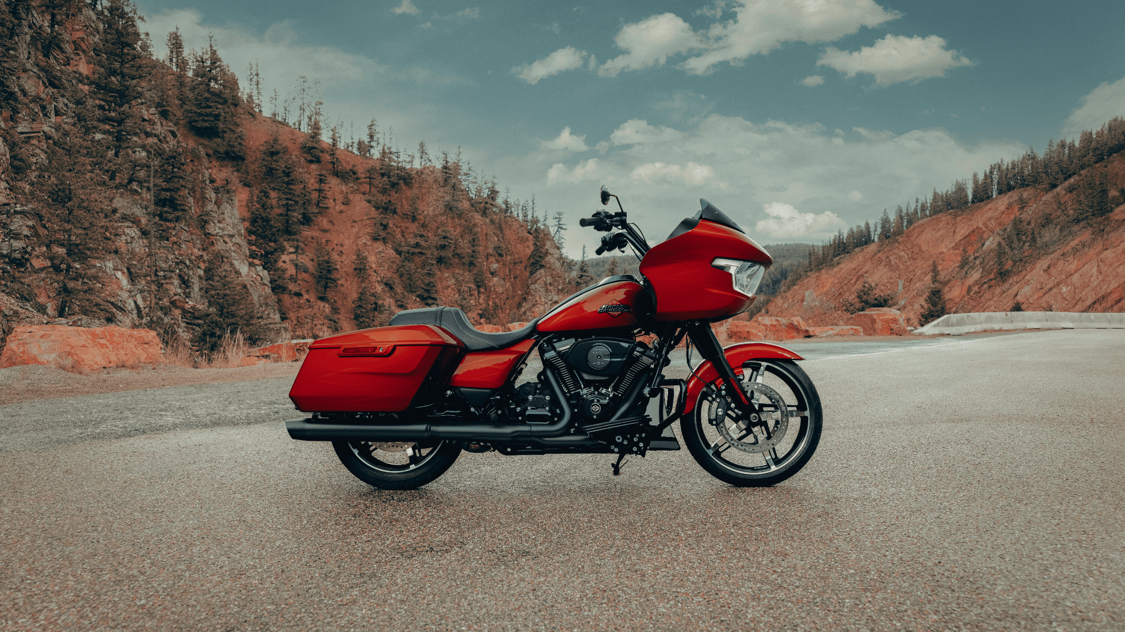 The 2025 Harley-Davidson® Road Glide® in bold red, parked against a rugged mountain backdrop, built…