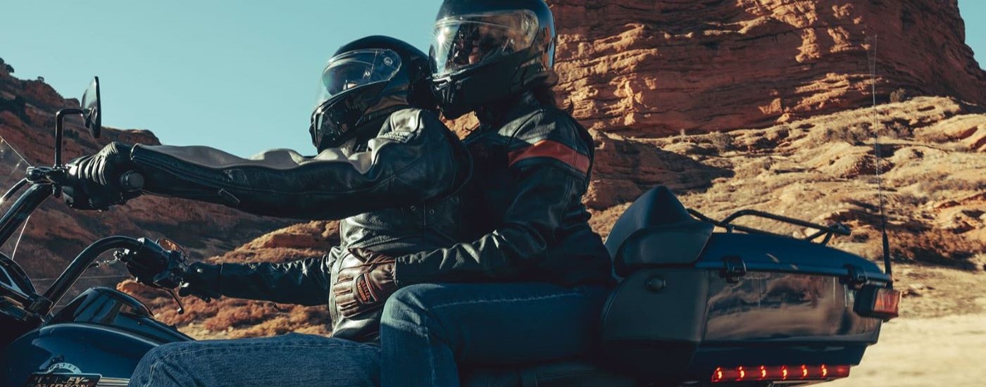 Two people are shown riding a black 2022 Harley-Davidson Road Glide Limited on a cunny day.