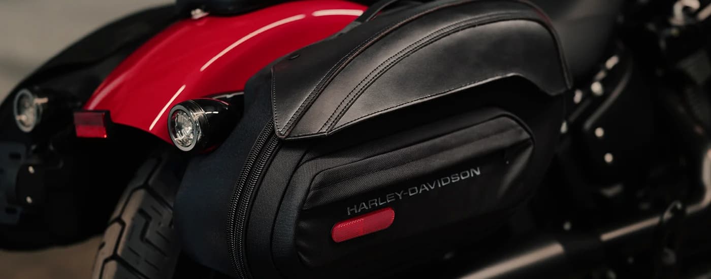 A close up of black leather saddlebags are shown on a red 2023 Harley-Davidson Street Bob 114. 