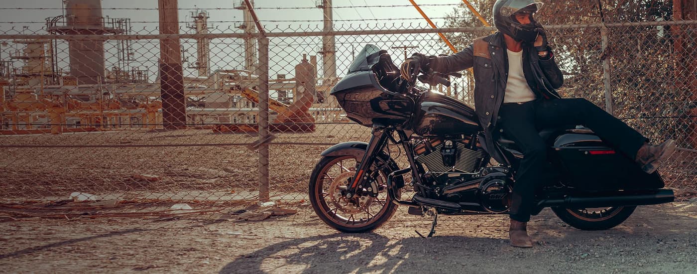 A man is shown sitting on a black 2023 Harley-Davidson Road Glide ST parked next to a fence.