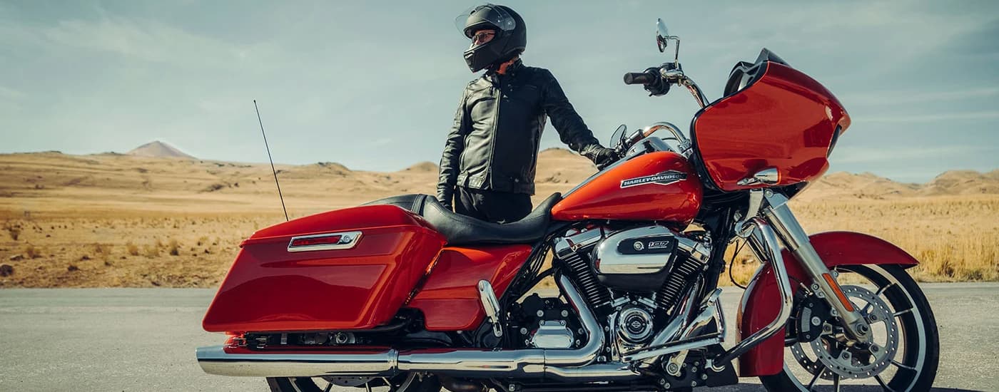 A man is shown standing next to a red Harley-Davidson Road Glide in a desert.