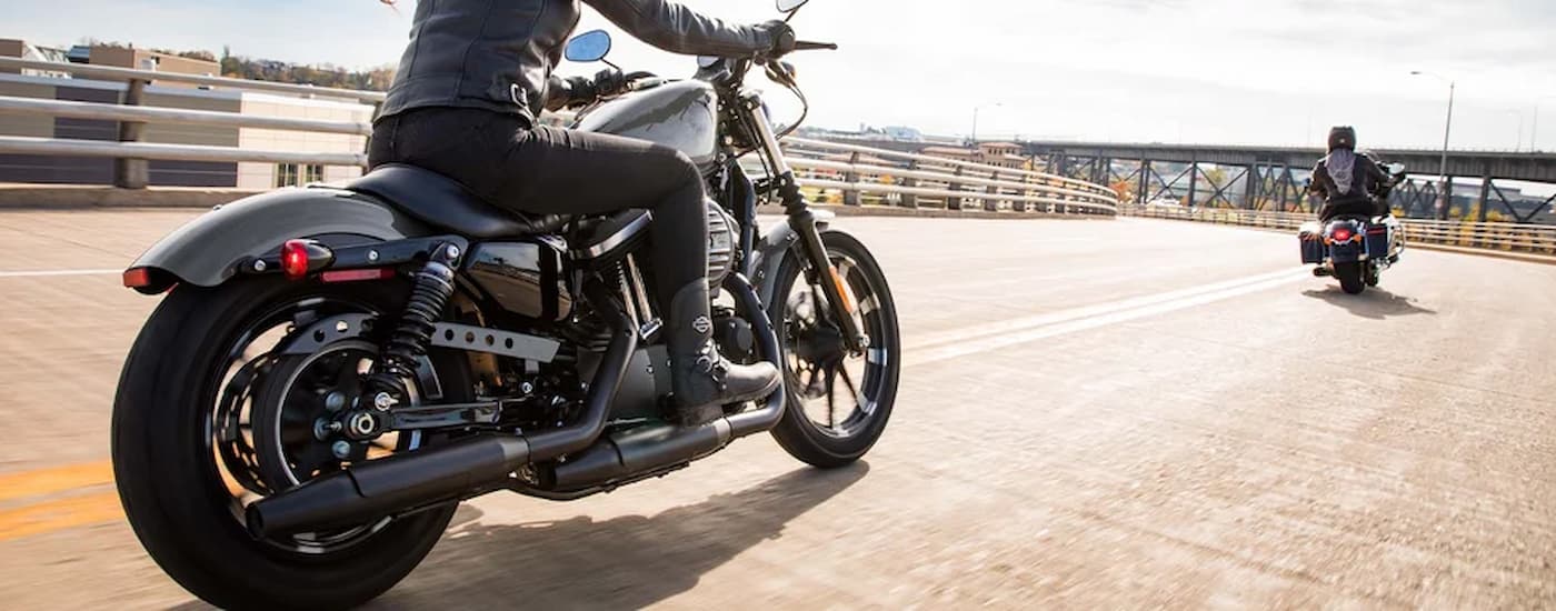 A black 2022 Harley-Davidson Iron 883 is shown driving across a bridge behind another motorcyclist.