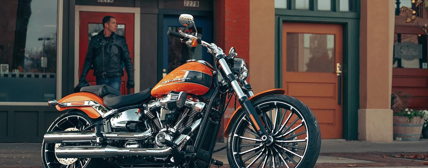 An orange 2023 Harley-Davidson Breakout 117 is shown parked in front of a coffee shop.